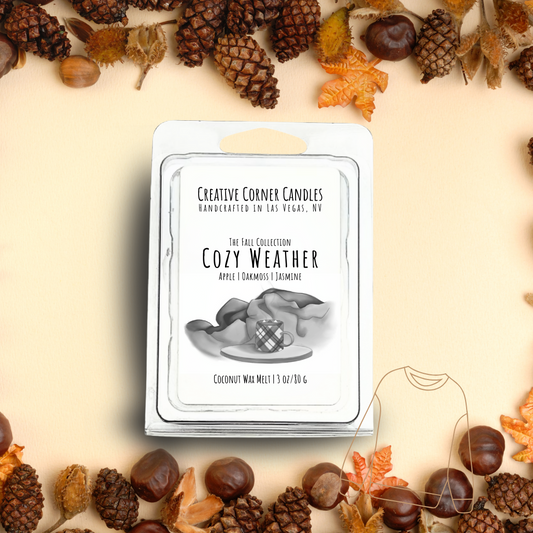 Cozy Weather wax melts with apple, oakmoss, and jasmine scent in coconut soy blend, hand-drawn label illustration of a coffee mug on wooden stand with blankets behind.