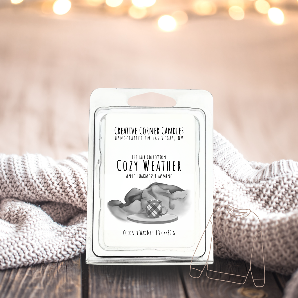 Cozy Weather wax melts with apple, oakmoss, and jasmine scent in coconut soy blend, hand-drawn label illustration of a coffee mug on wooden stand with blankets behind.
