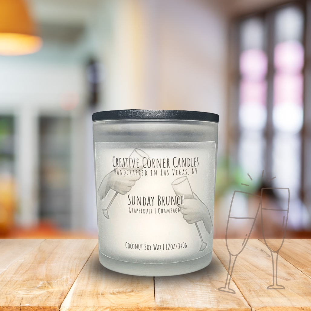 Sunday Brunch handcrafted candles with a fresh, uplifting scent and a label featuring a hand-drawn illustration of two hands holding champagne glasses in a cheers gesture