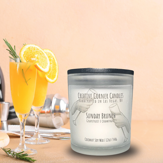 Sunday Brunch handcrafted candles with a fresh, uplifting scent and a label featuring a hand-drawn illustration of two hands holding champagne glasses in a cheers gesture