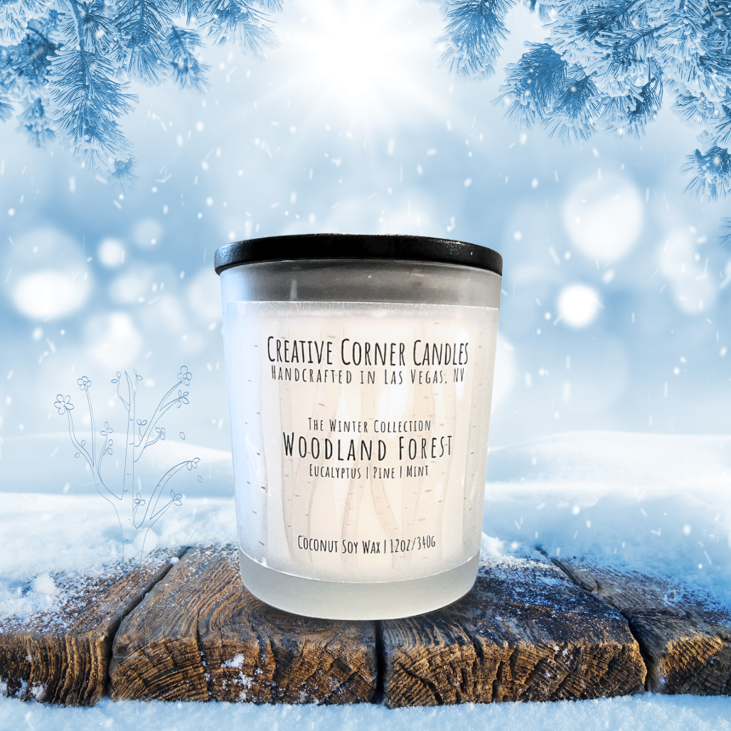 Candle labeled 'Woodland Forest' on a snowy background with tree branches.
