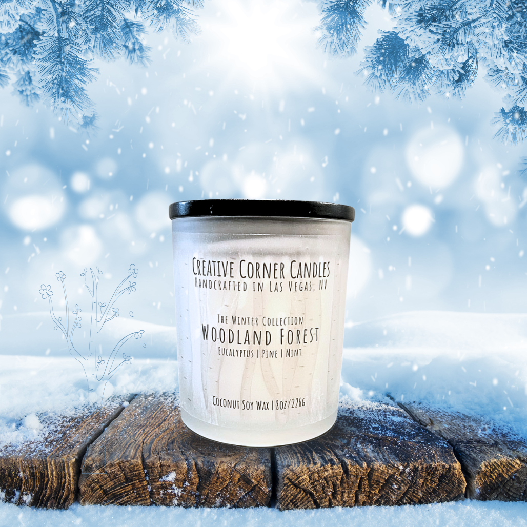 Candle labeled 'Woodland Forest' on a snowy background with tree branches.