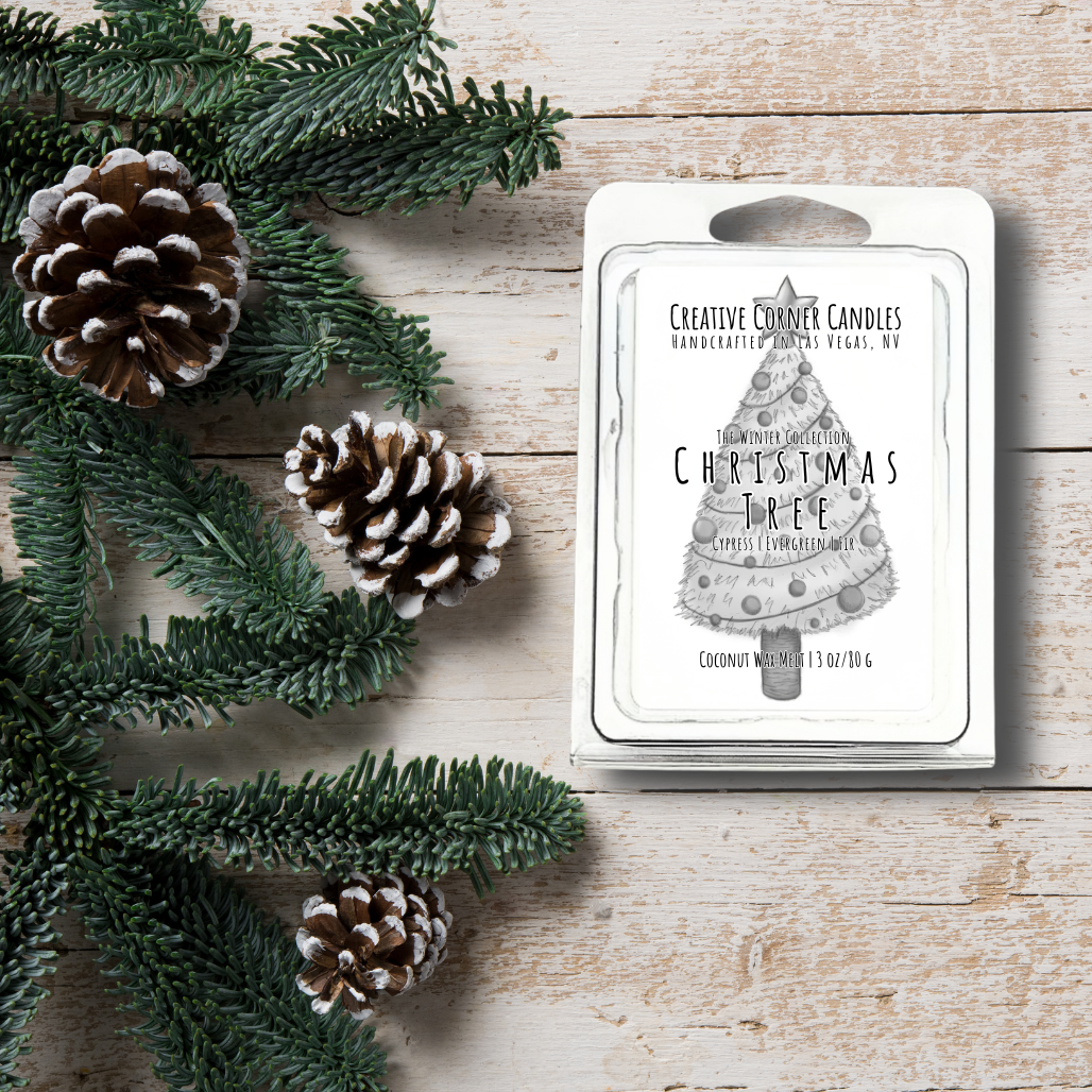 Christmas-themed candle packaging with pine cones and greenery on a wooden surface