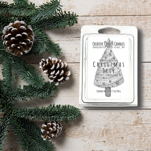 Christmas-themed candle packaging with pine cones and greenery on a wooden surface
