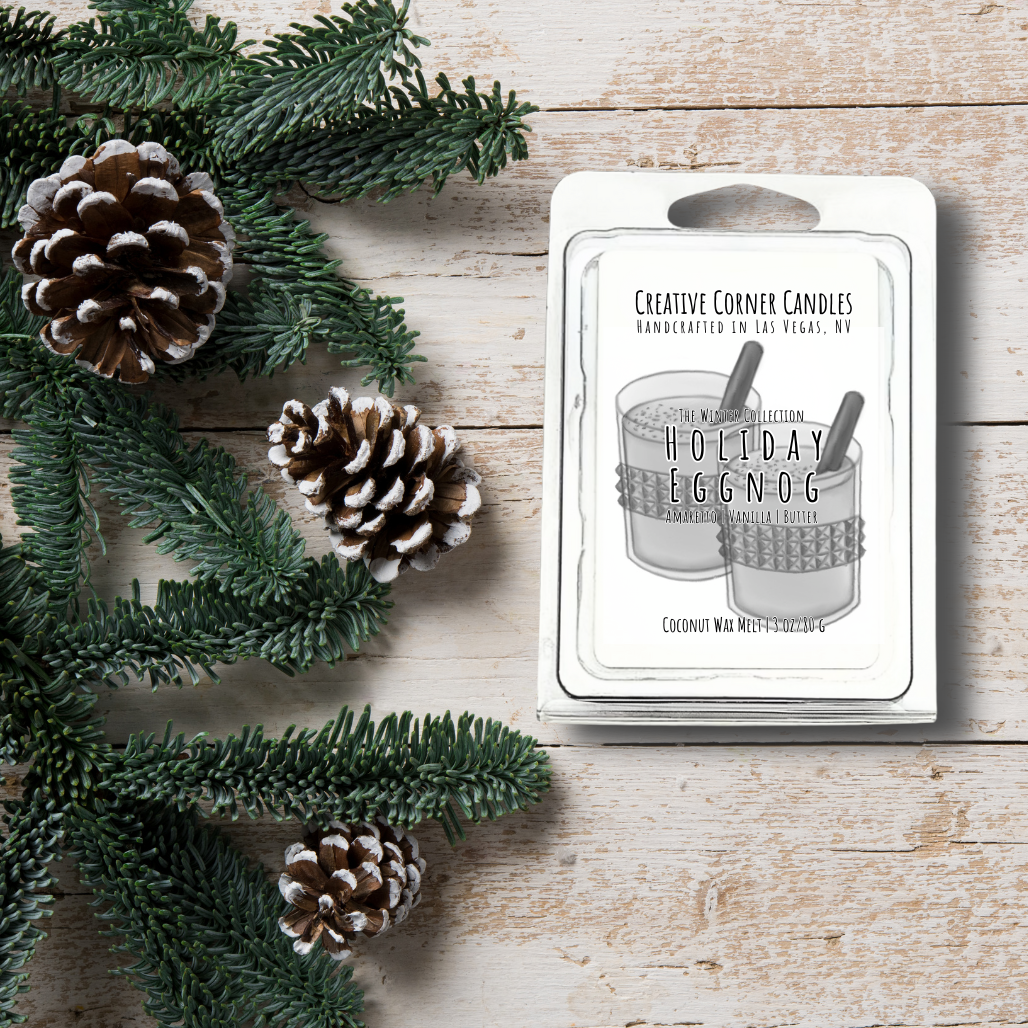 Candle packaging labeled 'Holiday Eggnog' with pine cones and greenery on a wooden surface