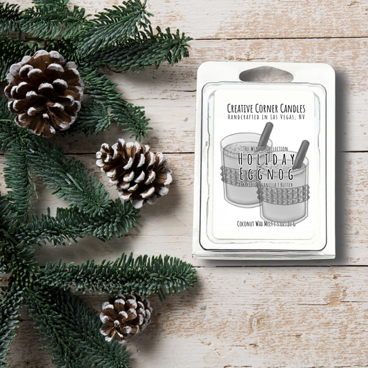 Candle packaging labeled 'Holiday Eggnog' with pine cones and greenery on a wooden surface