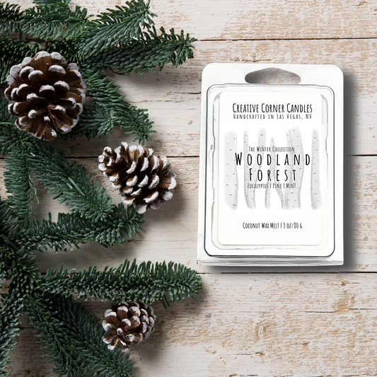 Wax melt packaging labeled 'Woodland Forest' with pine cones and greenery on a wooden surface