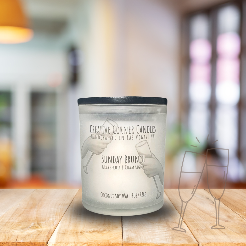 Sunday Brunch handcrafted candles with a fresh, uplifting scent and a label featuring a hand-drawn illustration of two hands holding champagne glasses in a cheers gesture